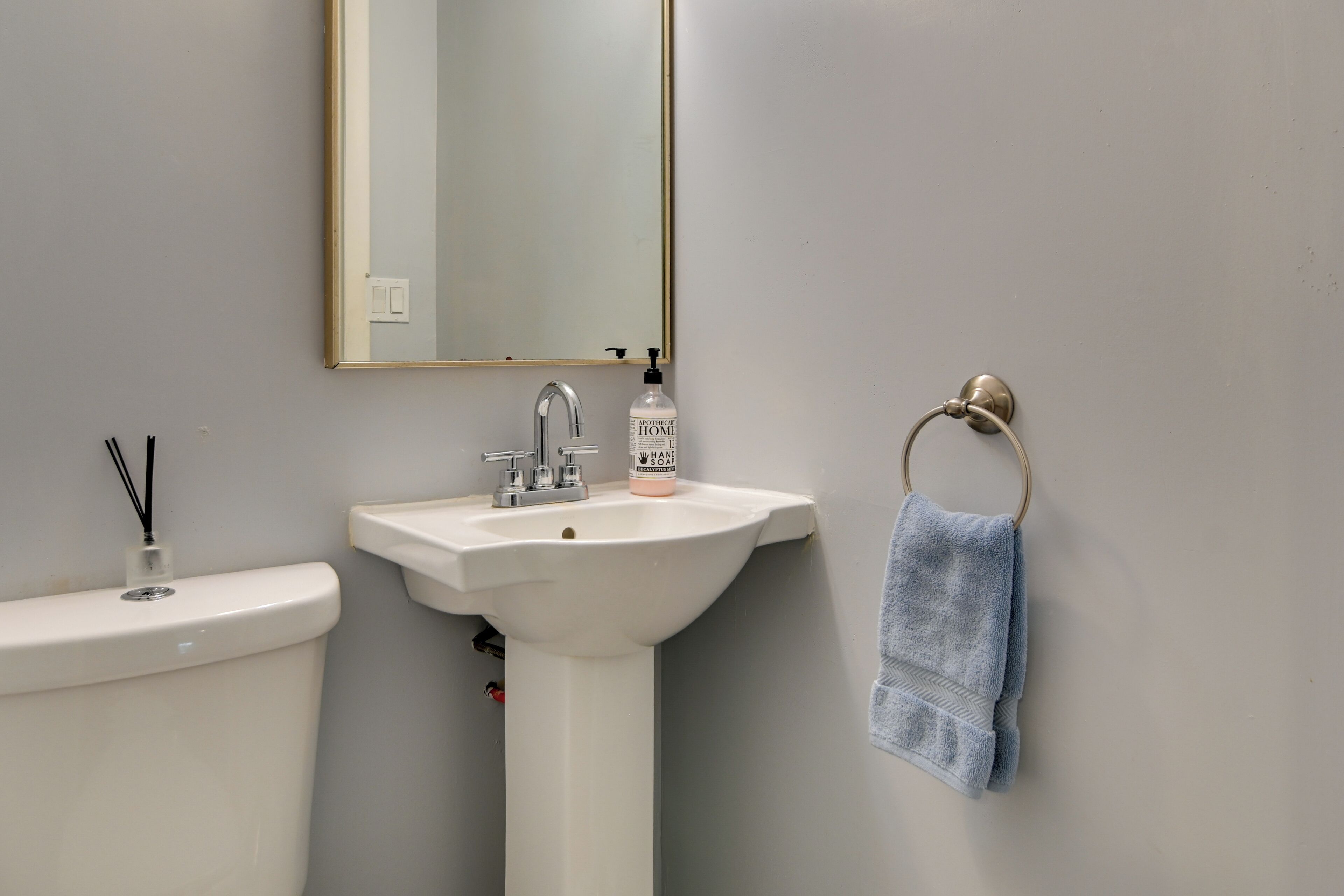Un baño con lavamanos blanco, un espejo y un perchero para toallas.