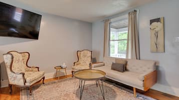 A living room with a sofa, two armchairs, a coffee table, a television, and a window with curtains.