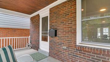 A covered porch with a brick wall, a white door, and a window.