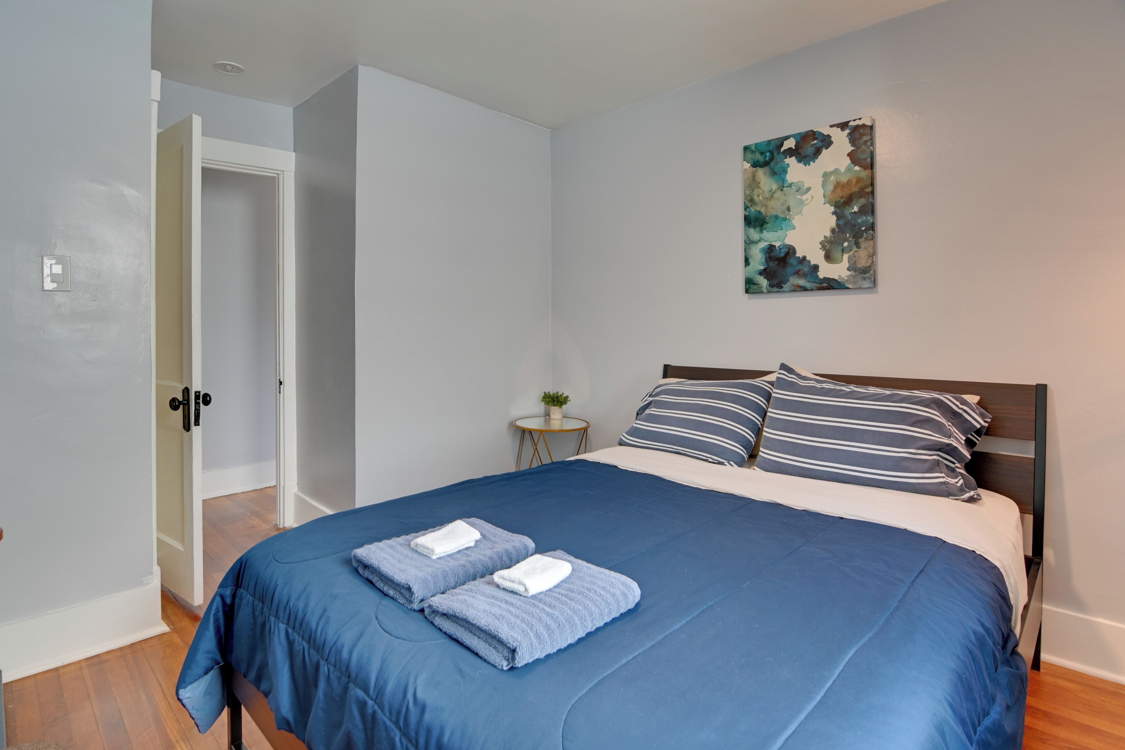 Un dormitorio con una cama, un cuadro y una mesita con una planta.