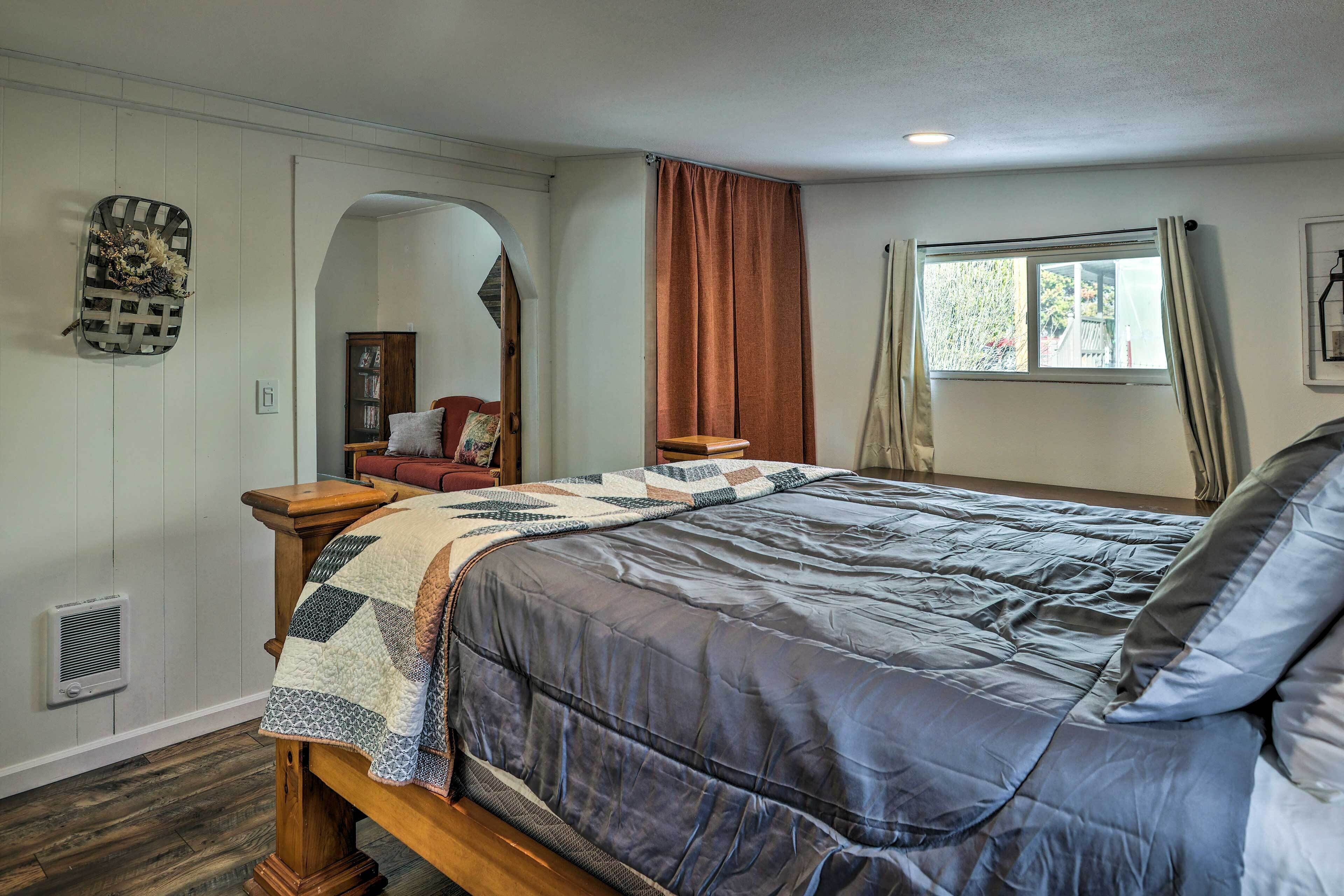Un dormitorio con cama, mesita de noche, cómoda, espejo, ventana con cortinas y un adorno en la pared.