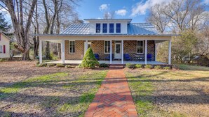 A single-story house with a brick exterior, a covered porch with blue chairs, and a brick pathway leading to the entrance. - Radiant Gloucester House w/ Private Porch! (Gloucester)