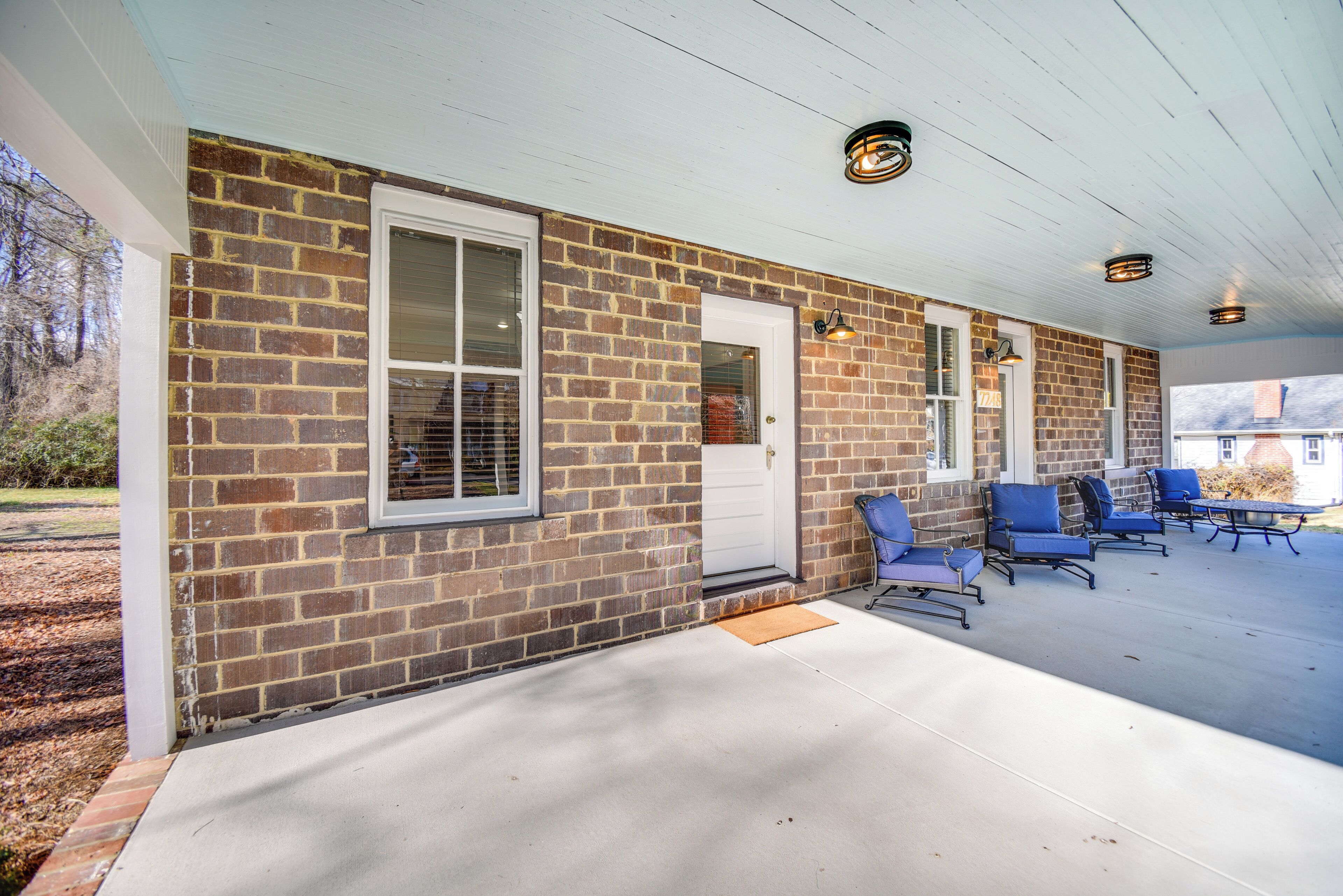 A brick building with a covered porch, a white door, and blue chairs.