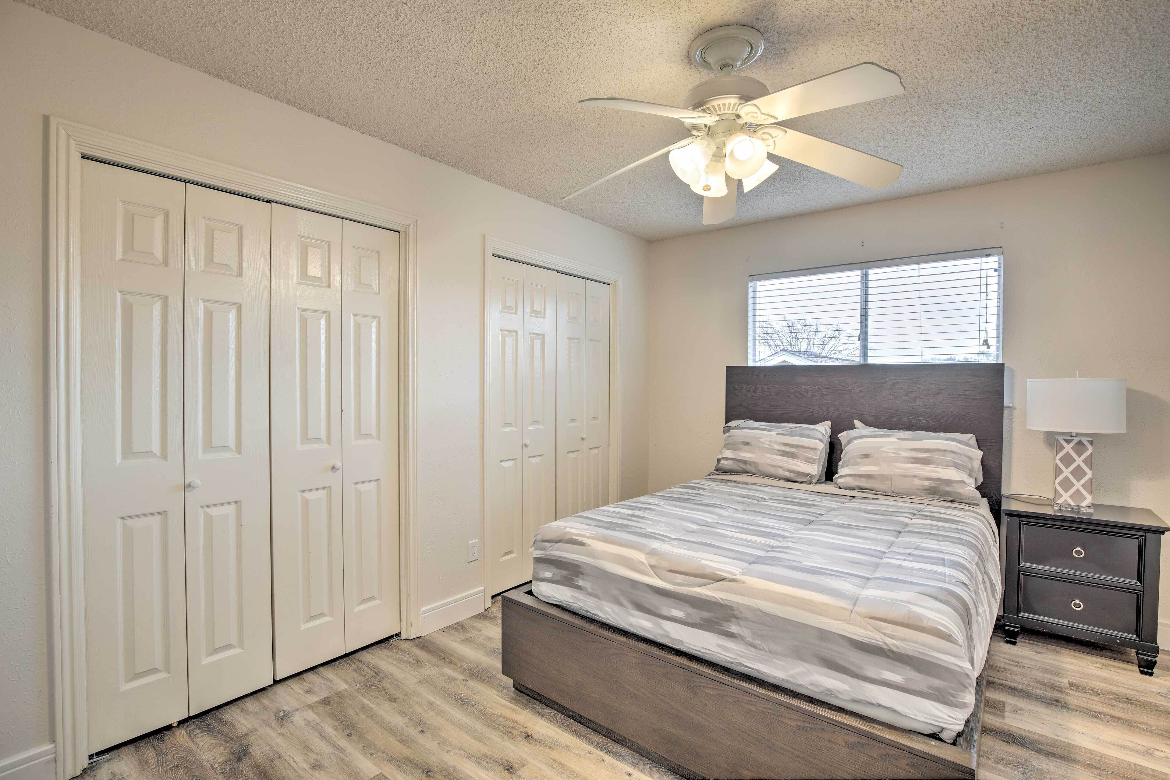 A bedroom with a bed, a ceiling fan, a window, and a nightstand.