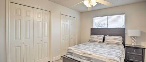 A bedroom with a bed, a ceiling fan, a window, and a nightstand.