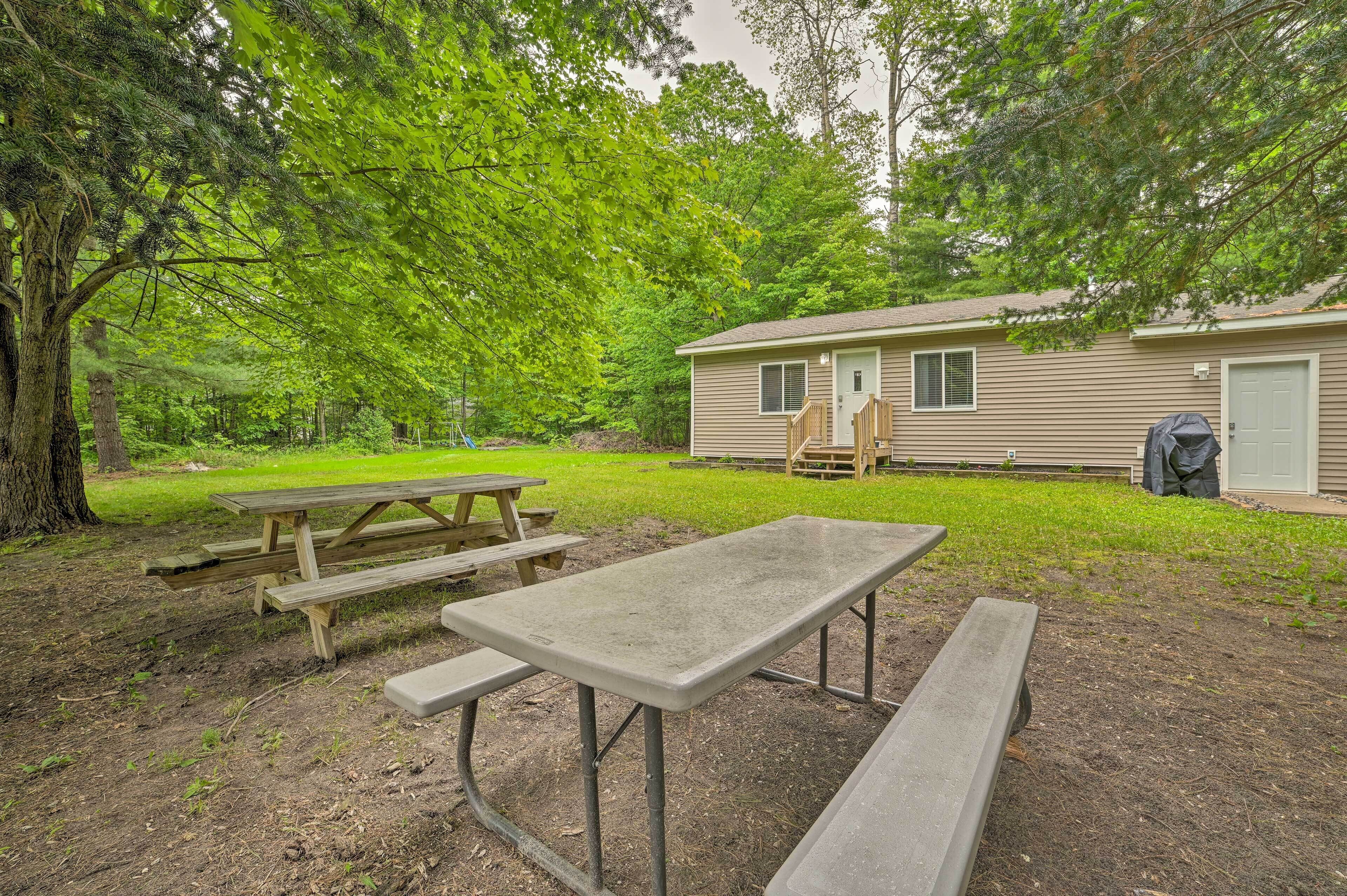 Een picknicktafel en bankjes in een grasveld, met een huis op de achtergrond.