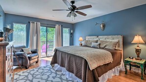 Ein Schlafzimmer mit einem Bett, einem Deckenventilator, einem Nachttisch, einem Sessel und einem Fenster mit Vorhängen.
