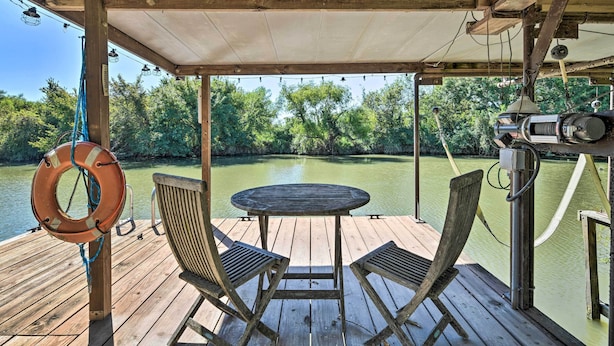 Eine Holzterrasse mit Tisch und Stühlen bietet Blick auf einen ruhigen Fluss, umgeben von üppigem Grün.