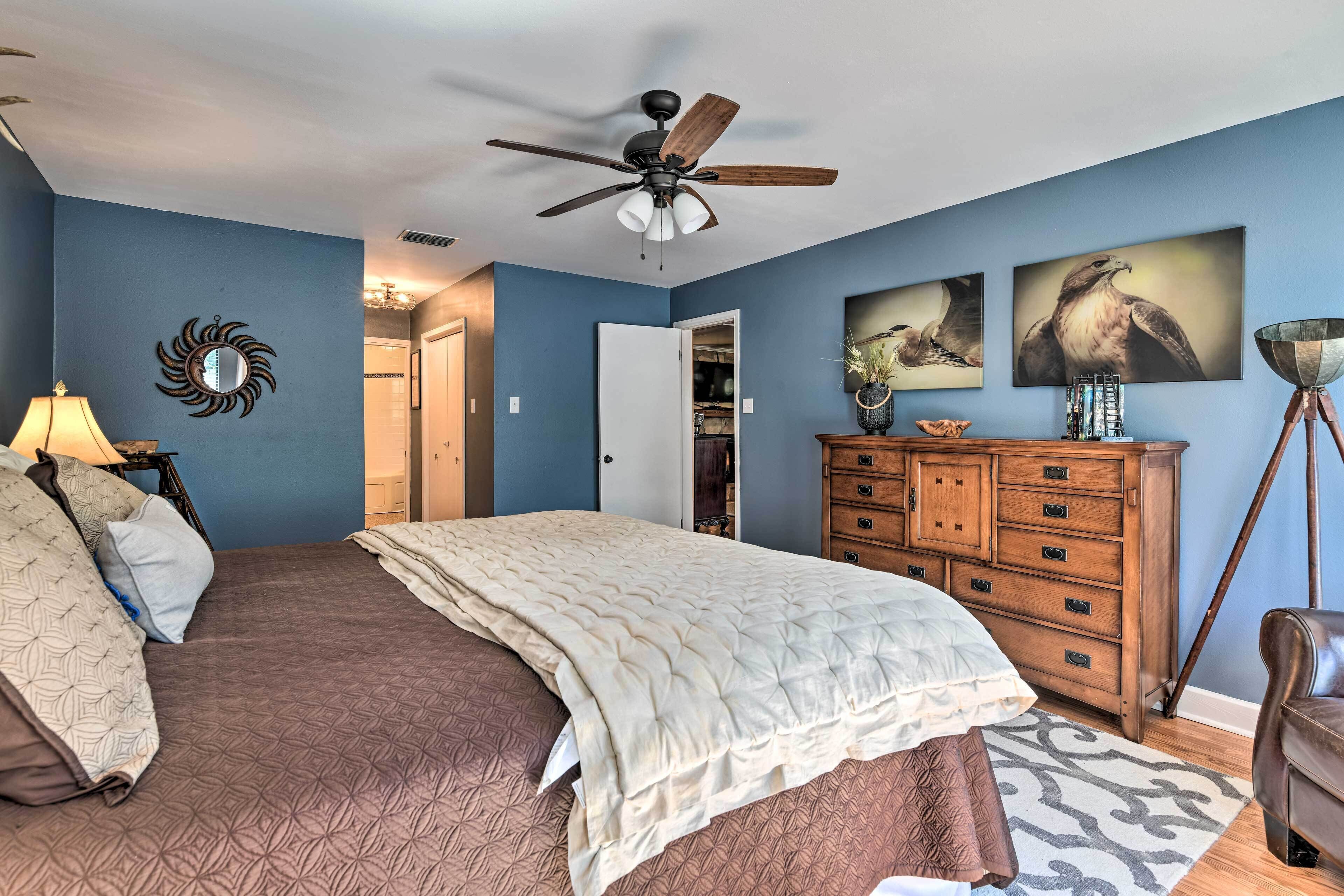 A bedroom with a bed, a ceiling fan, a dresser, and artwork on the walls.