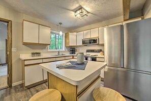 A modern kitchen with white cabinetry, a central island, stainless steel appliances, and a window providing natural light. - Higgins Lake Getaway - Boating, Fish, Golf, Atv! (Roscommon)