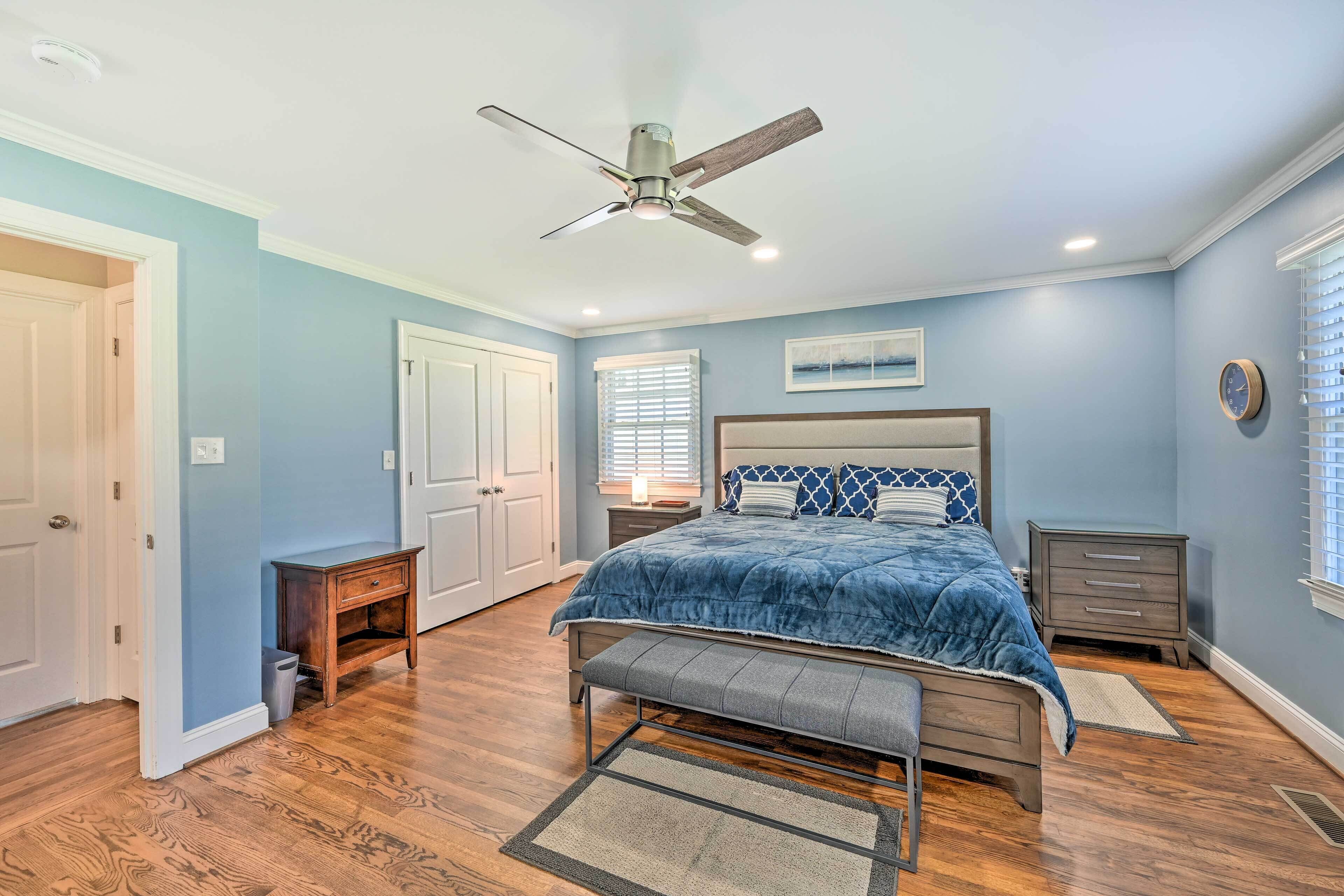 A bedroom with a bed, a bench, a nightstand, a ceiling fan, and a window with blinds.