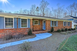 A single-story brick house with a front porch, a small front yard, and a clear sky. - Ranch-style Home 7 Mi to Downtown Greensboro! (Greensboro)