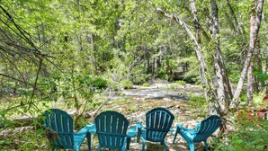 Een natuurlijke omgeving met een rivier, omringd door bomen en groen, met terrasmeubilair met stoelen en tafels.