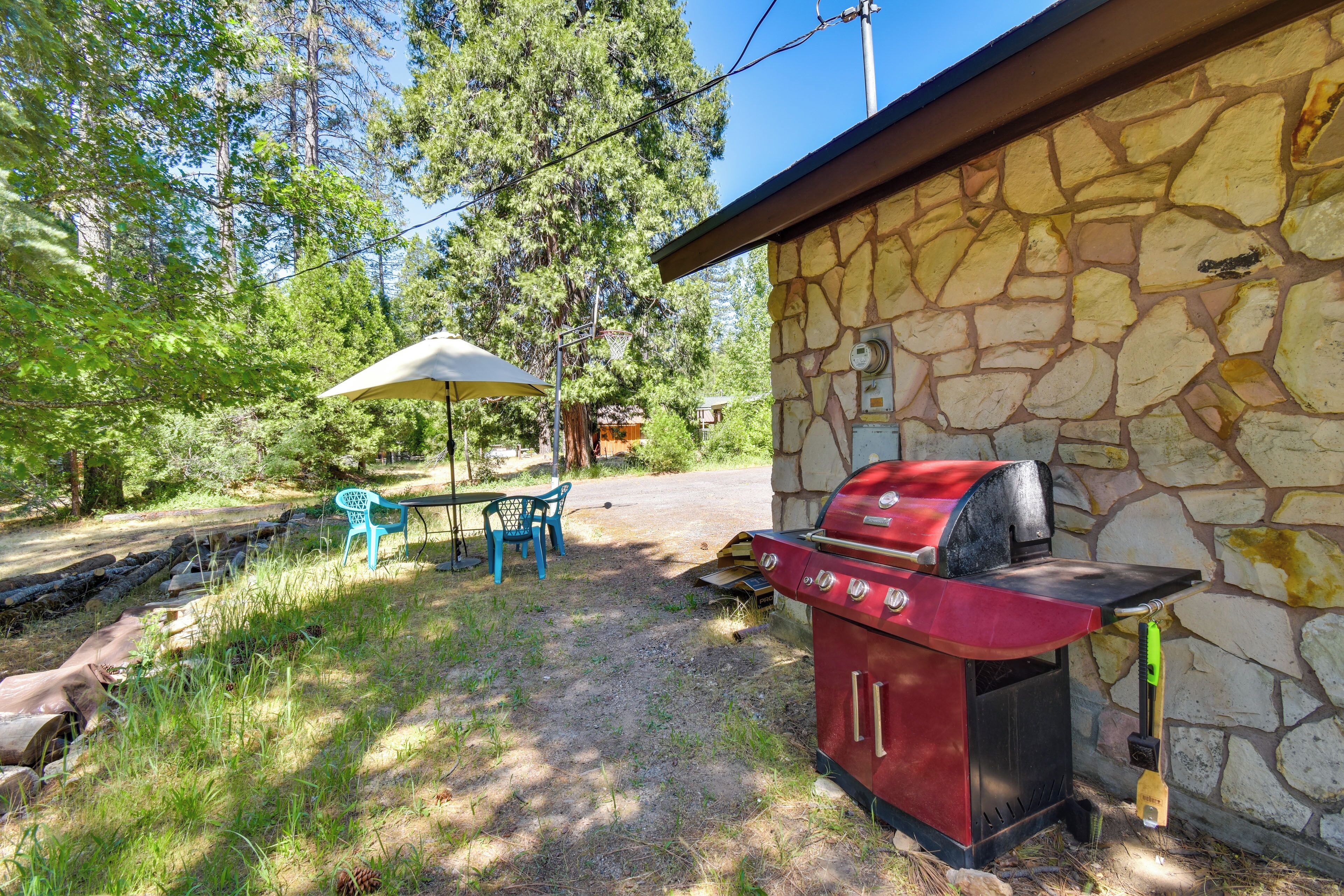 A stone building with a barbecue grill, outdoor seating with a table and chairs, and a picnic table under a canopy.
