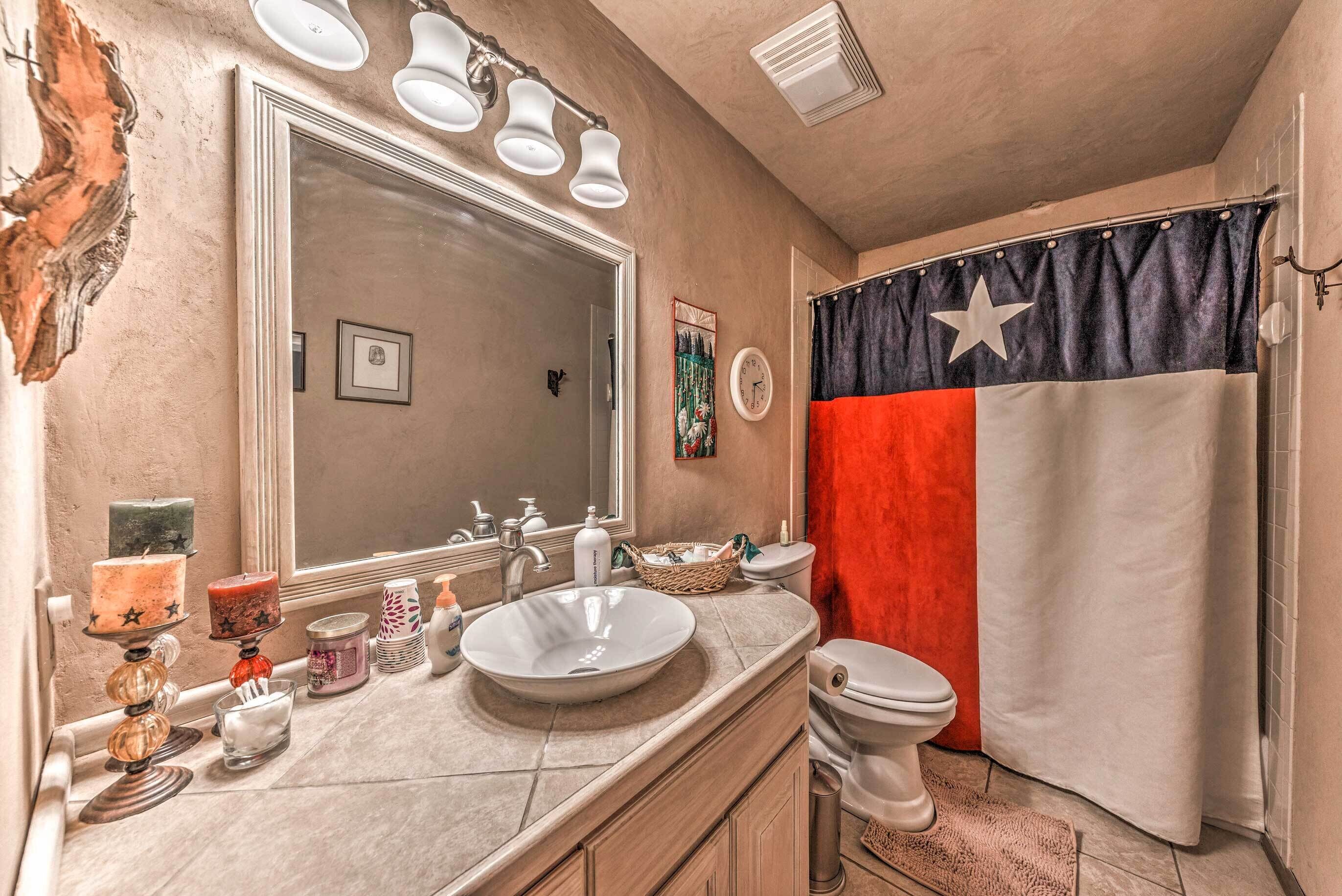 A bathroom with a large mirror, a sink, a toilet, and a shower curtain with a flag design.
