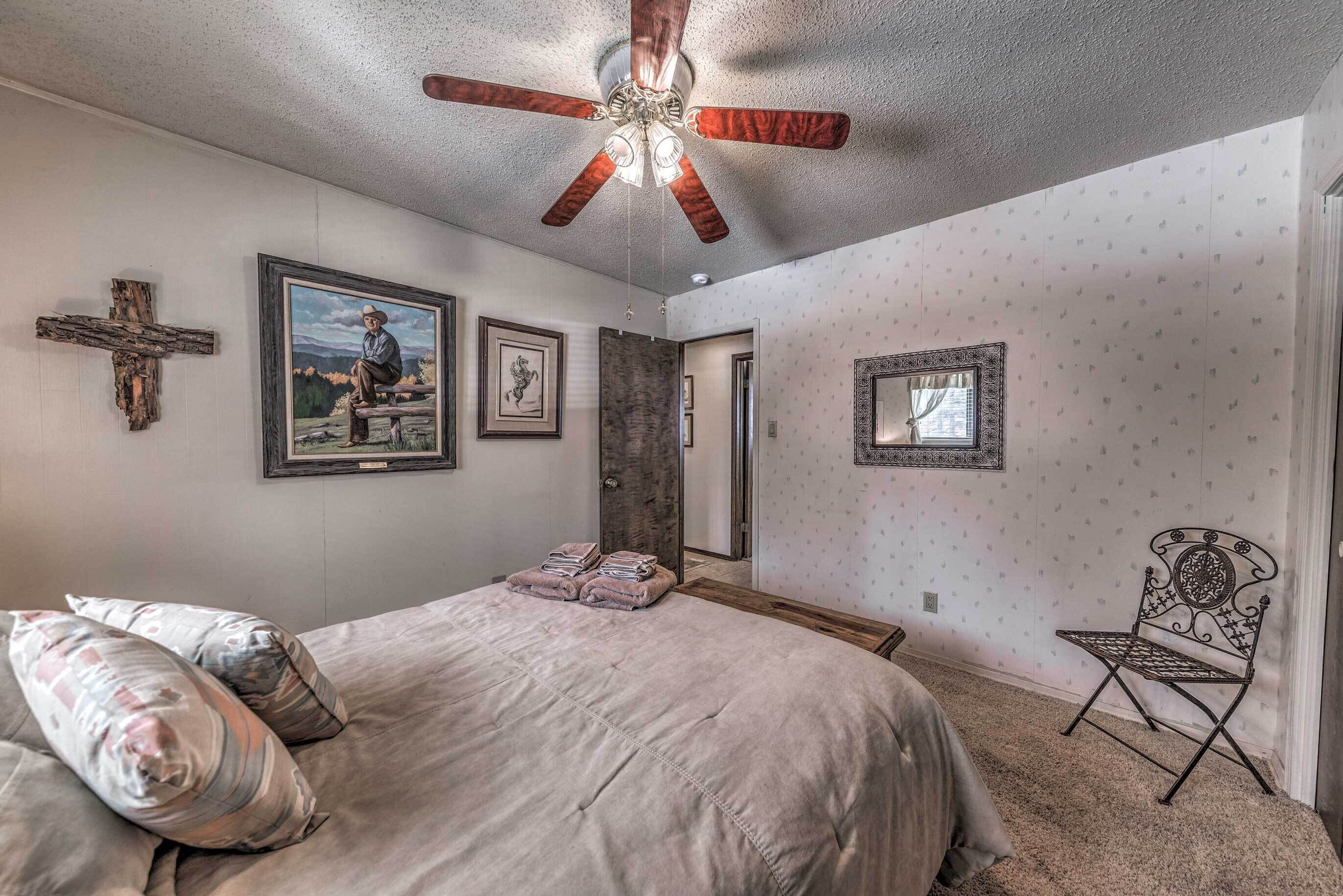Ein Schlafzimmer mit einem Bett, einem Deckenventilator, einem Kreuz an der Wand und gerahmten Bildern.