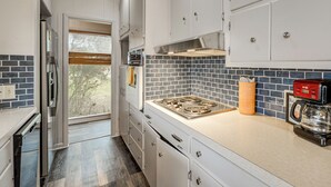 Une cuisine moderne avec des meubles blancs, une hotte de cuisinière en acier inoxydable, une machine à café et une fenêtre équipée de stores.