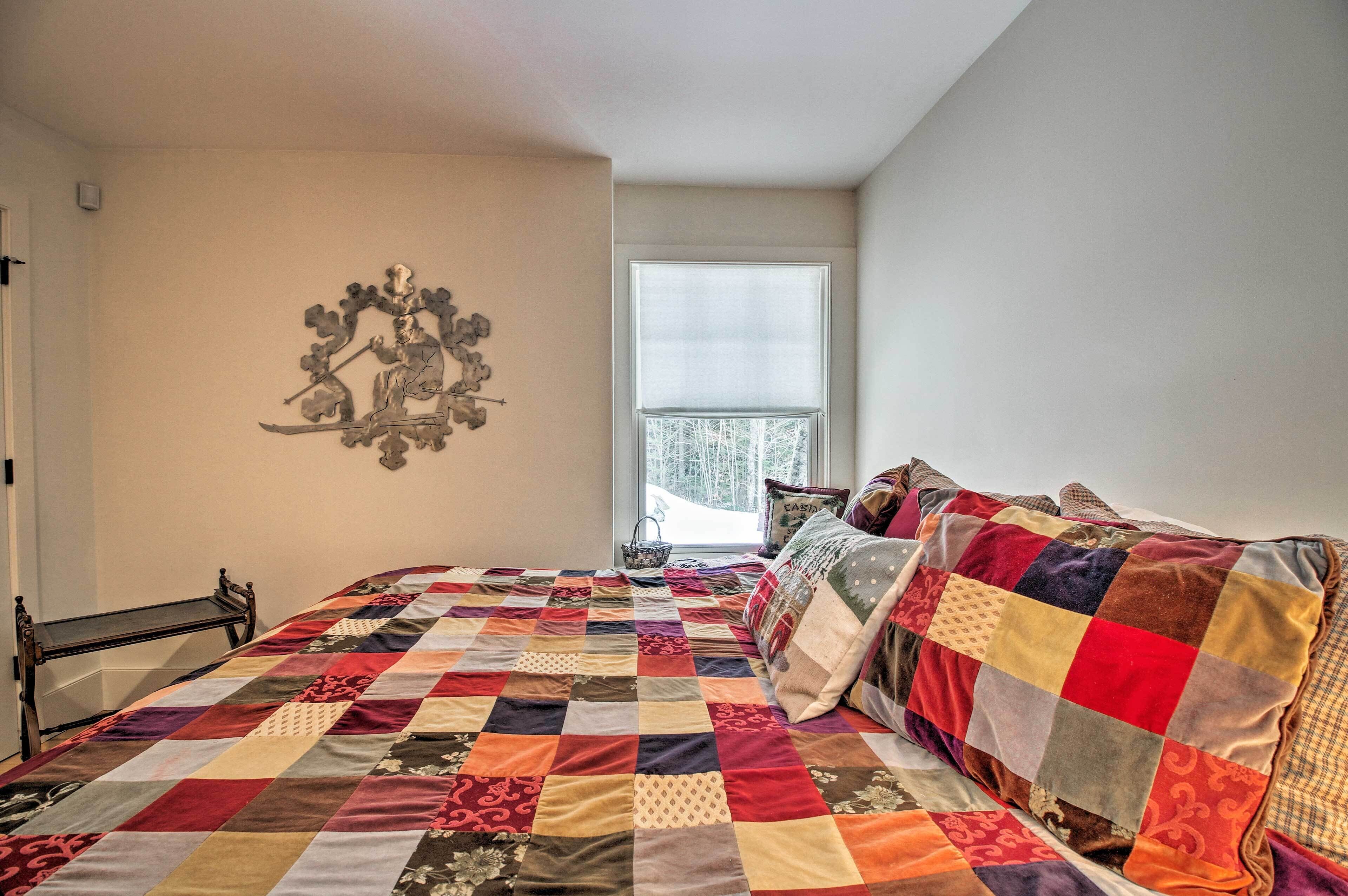 A bedroom with a large bed, a window with blinds, a wall-mounted artwork, and a bedside table.