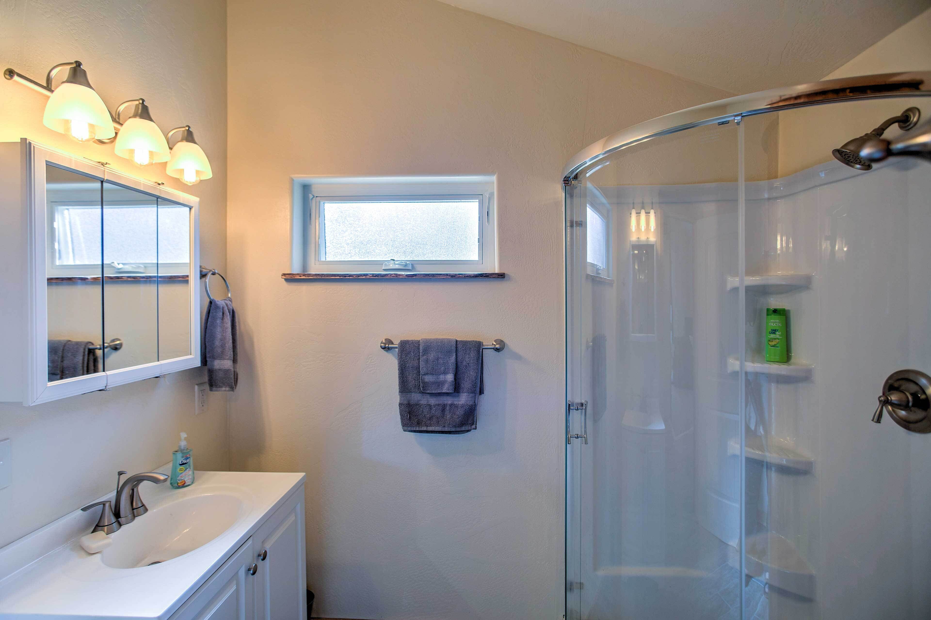 A bathroom with a sink, mirror, towel rack, and a glass-enclosed shower.