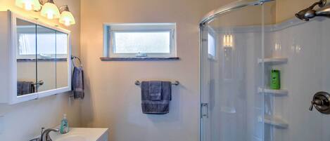 A bathroom with a sink, mirror, towel rack, and a glass-enclosed shower.