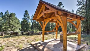 A wooden gazebo with a sloped roof, supported by wooden beams, situated on a stone platform in a forested area. - Mancos Cabin Rental on 80 Acres w/ Mountain View! (Mancos)