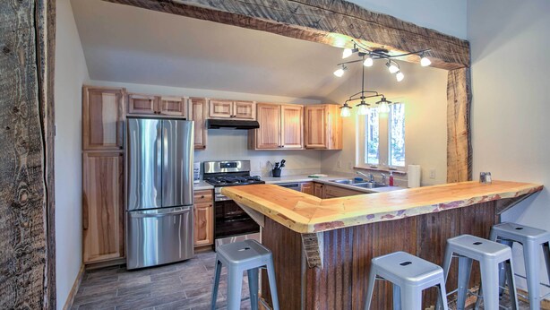 A modern kitchen with wooden cabinets, stainless steel appliances, and a bar area with stools. - Mancos Cabin Rental on 80 Acres w/ Mountain View! (Mancos)