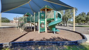 Un parque infantil con tobogán, estructuras para escalar y una zona con sombra.