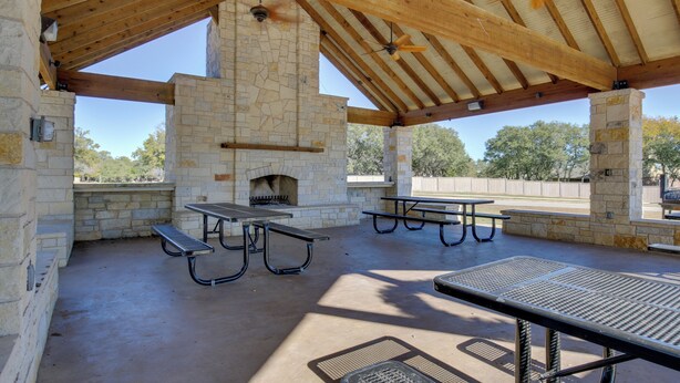 Un patio exterior con paredes de piedra, vigas de madera y mesas de picnic.