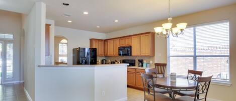 A spacious kitchen with a central island, wooden cabinets, and a dining area with chairs.