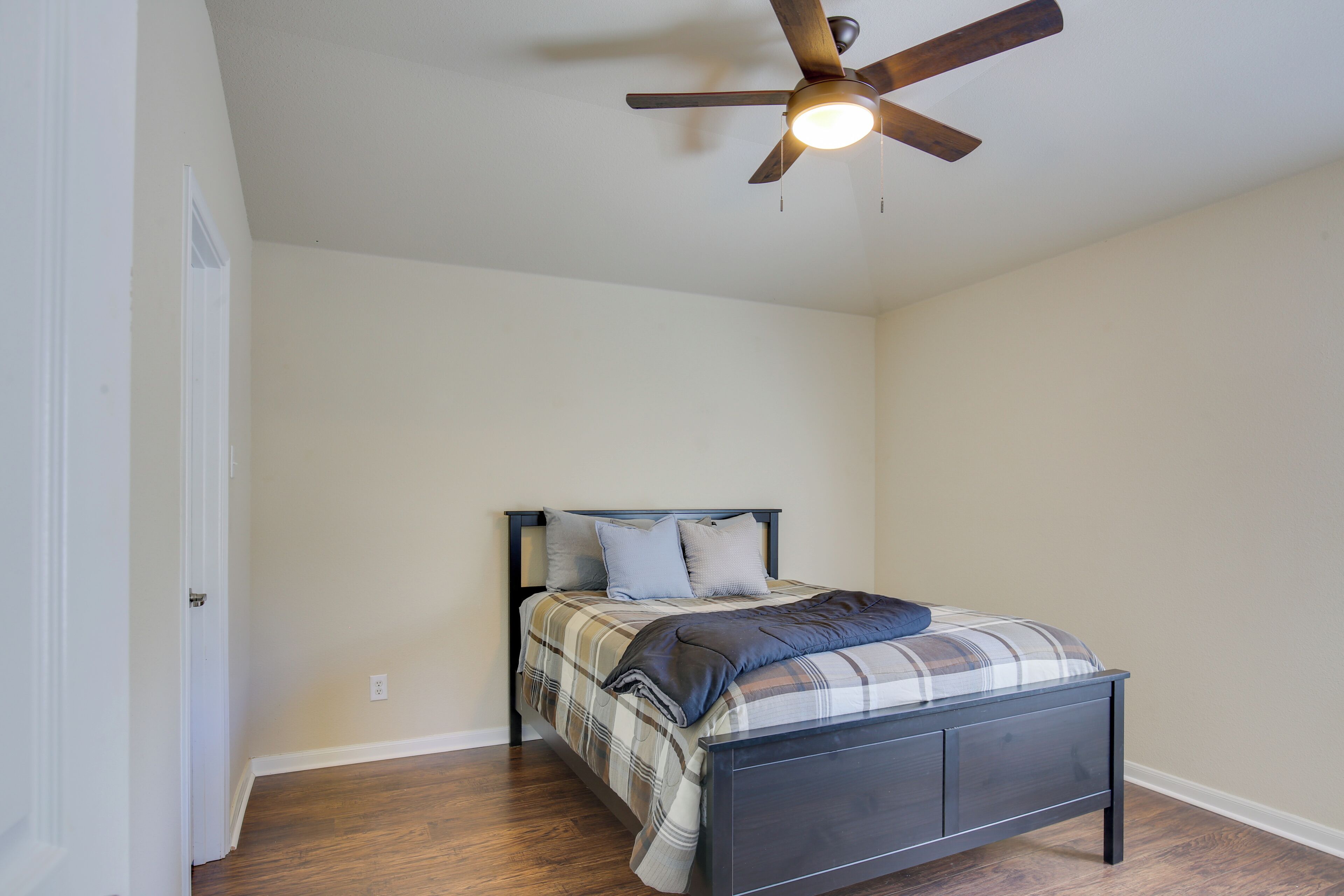 A bedroom with a bed, a ceiling fan, and wooden flooring.
