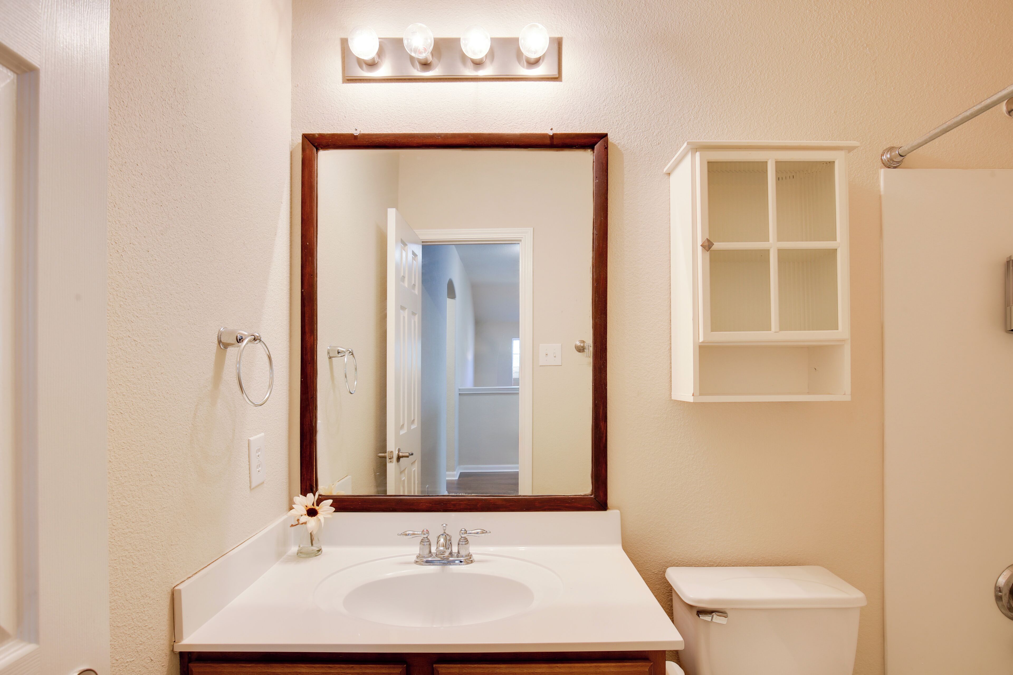 Un bagno con un lavandino bianco, uno specchio illuminato, un water e un armadietto.