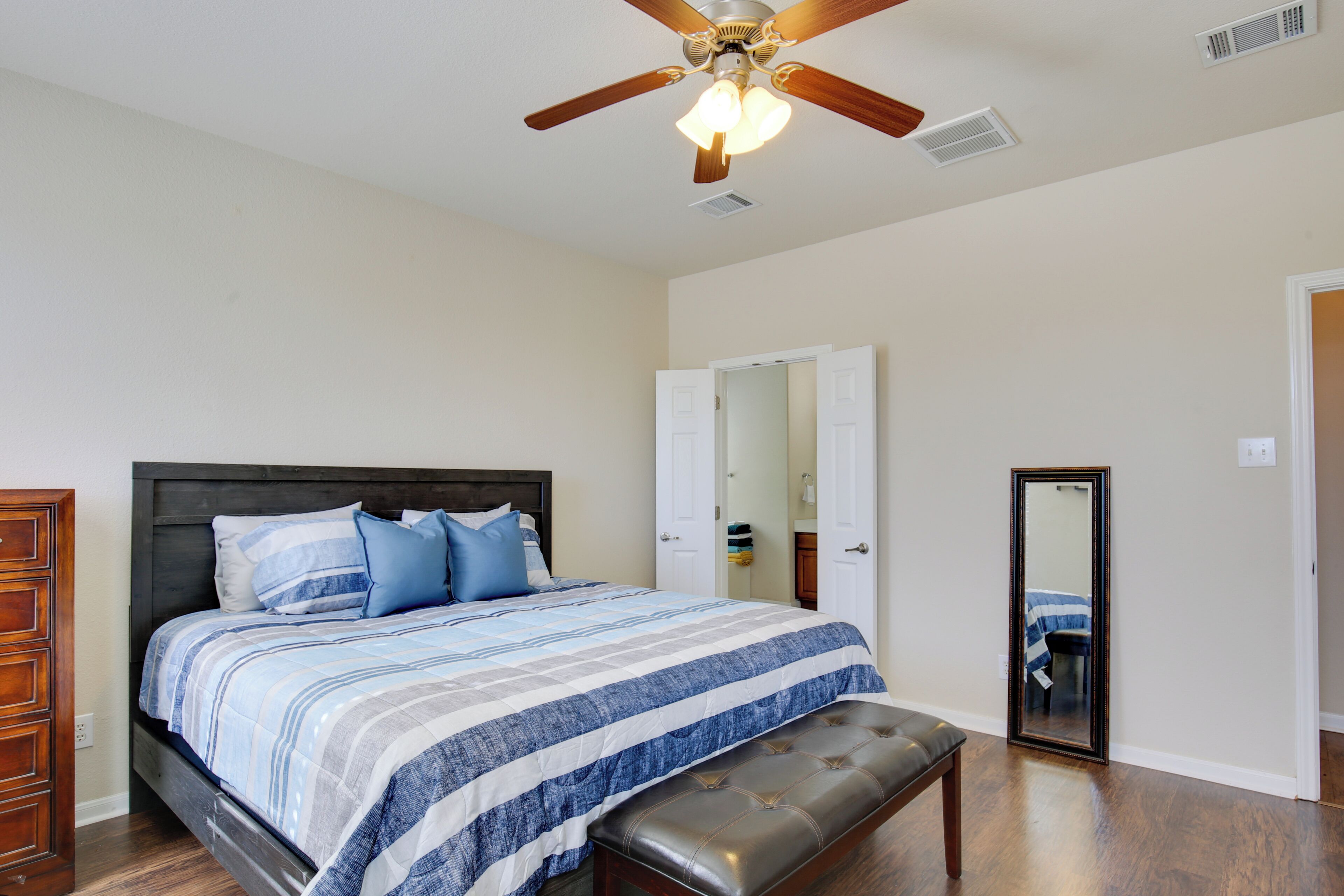 A bedroom with a bed, a bench, a ceiling fan, and a door.