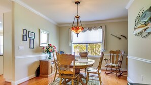 A dining area with a round table, wooden chairs, a chandelier, a patterned rug, and a window with curtains. - 4 Mi to Fenwick Island: Home w/ Pool Access & Deck (Selbyville)