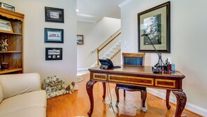 A living room with a wooden coffee table, a sofa, and a dog. There are framed pictures on the wall and a staircase in the background. - 4 Mi to Fenwick Island: Home w/ Pool Access & Deck (Selbyville)