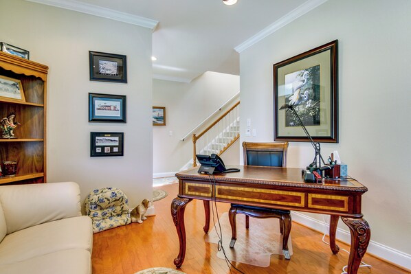 A living room with a wooden coffee table, a sofa, and a dog. There are framed pictures on the wall and a staircase in the background. - 4 Mi to Fenwick Island: Home w/ Pool Access & Deck (Selbyville)