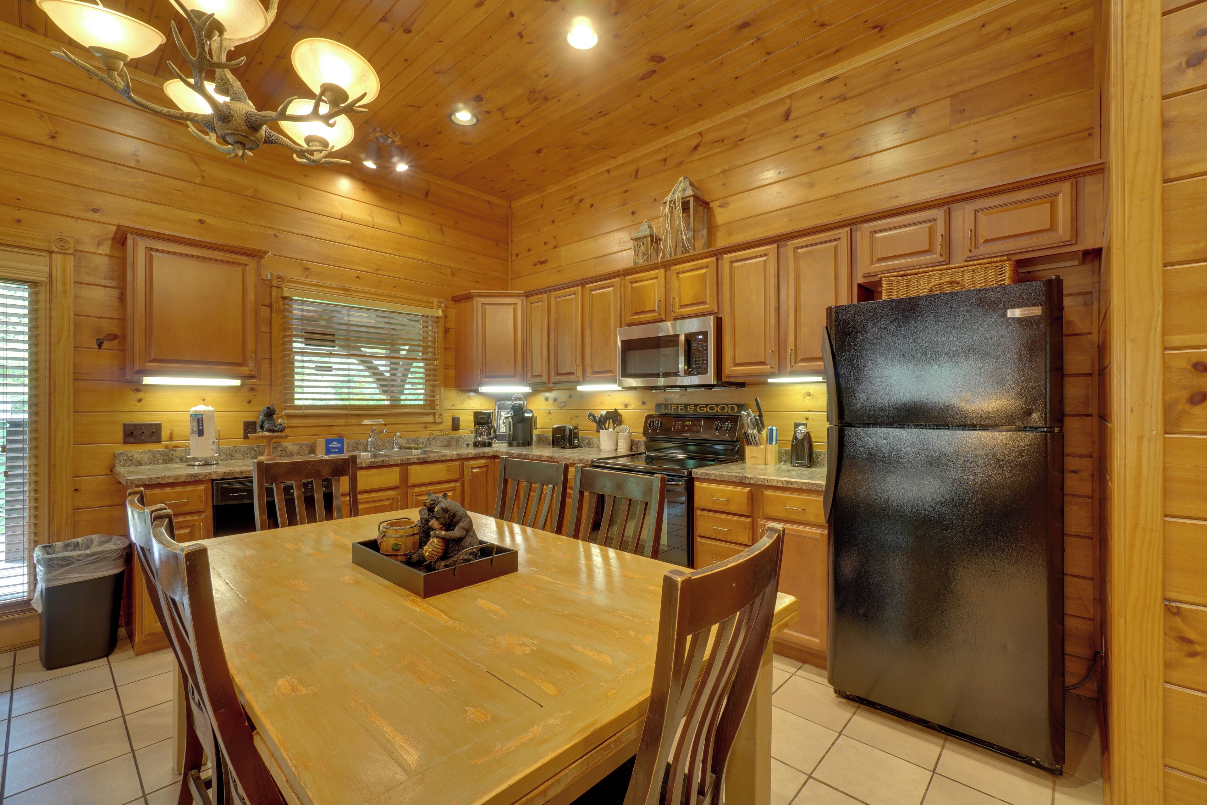 A wooden cabin-style kitchen with a dining table, chairs, a refrigerator, and a microwave.