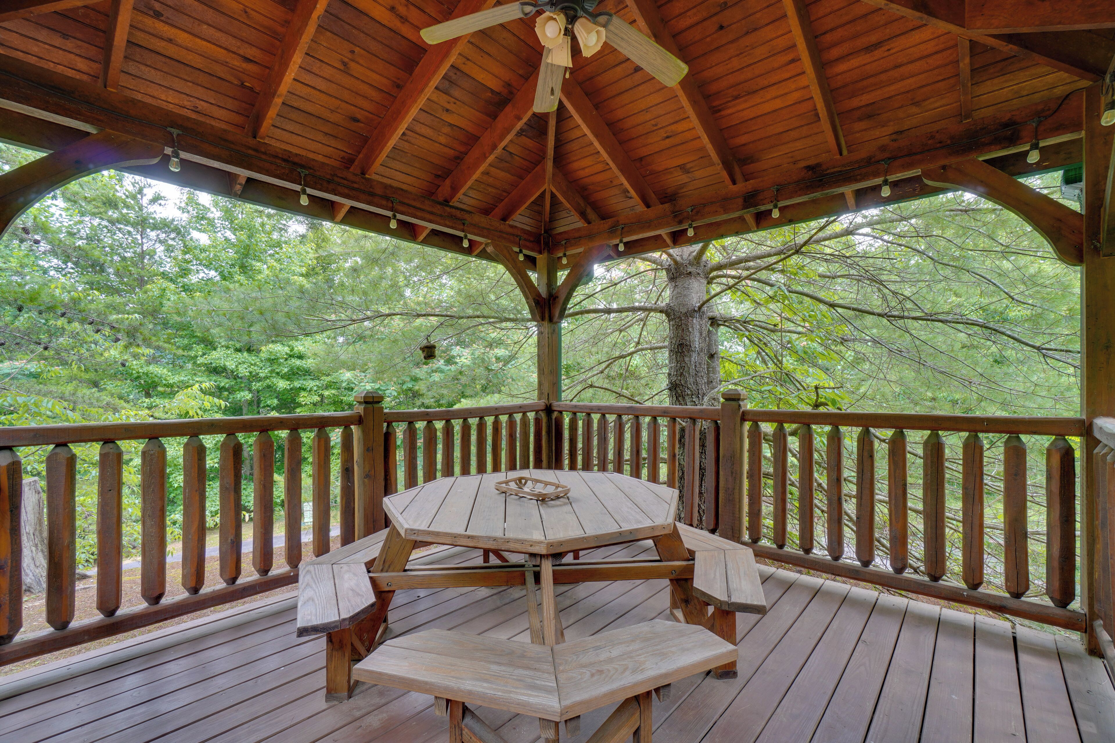 A wooden deck with a table and benches, surrounded by a railing, overlooking a forested area.