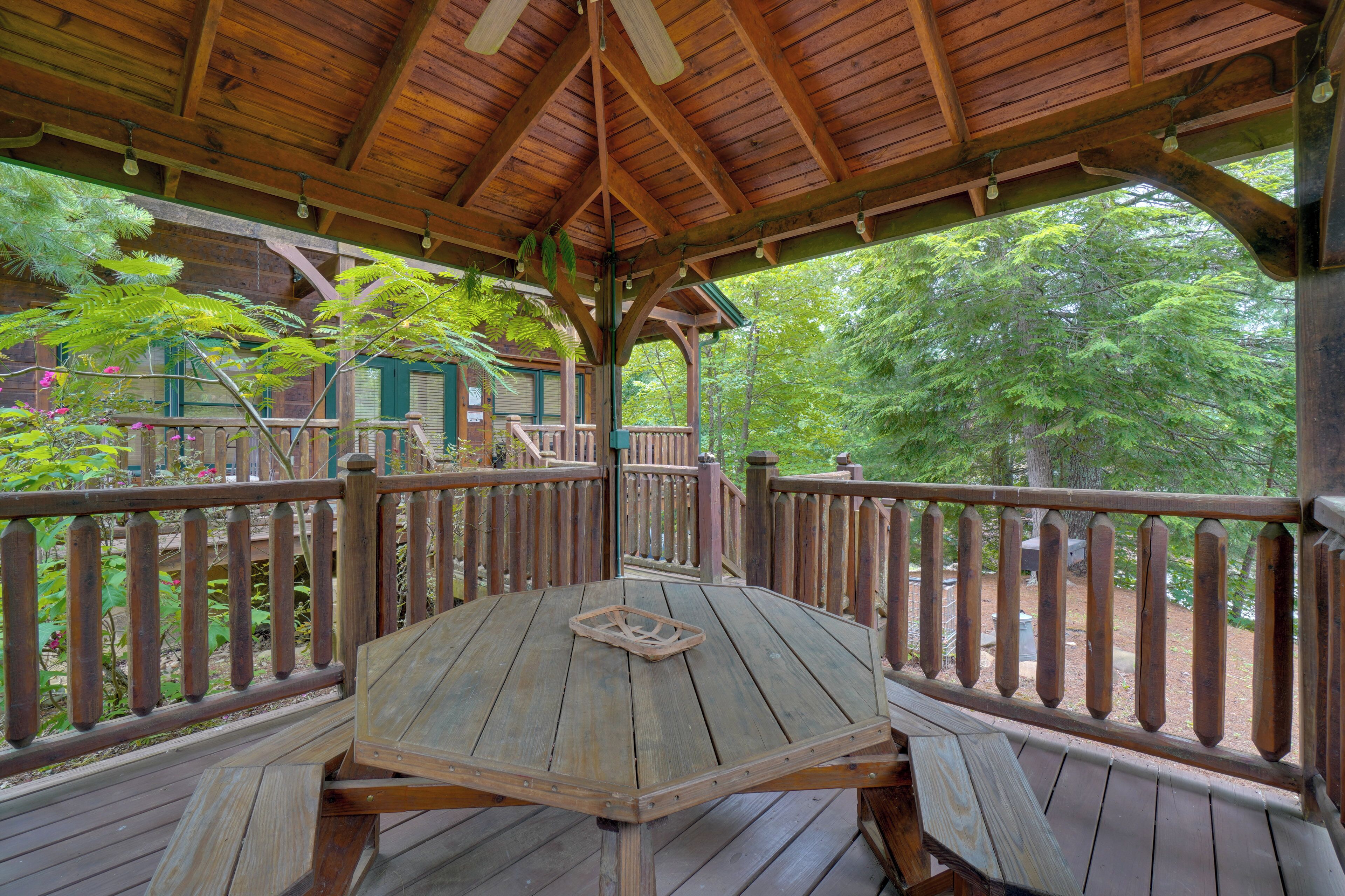A wooden deck with a table and benches, surrounded by a wooden railing, overlooking a forested area.