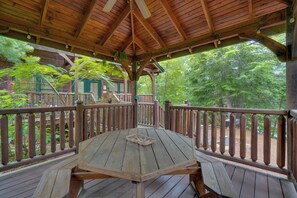 A wooden deck with a table and benches, surrounded by a wooden railing, overlooking a forested area. - Hot Tub & Deck: Cabin Near Smoky Mtn Trails! (Sevierville)