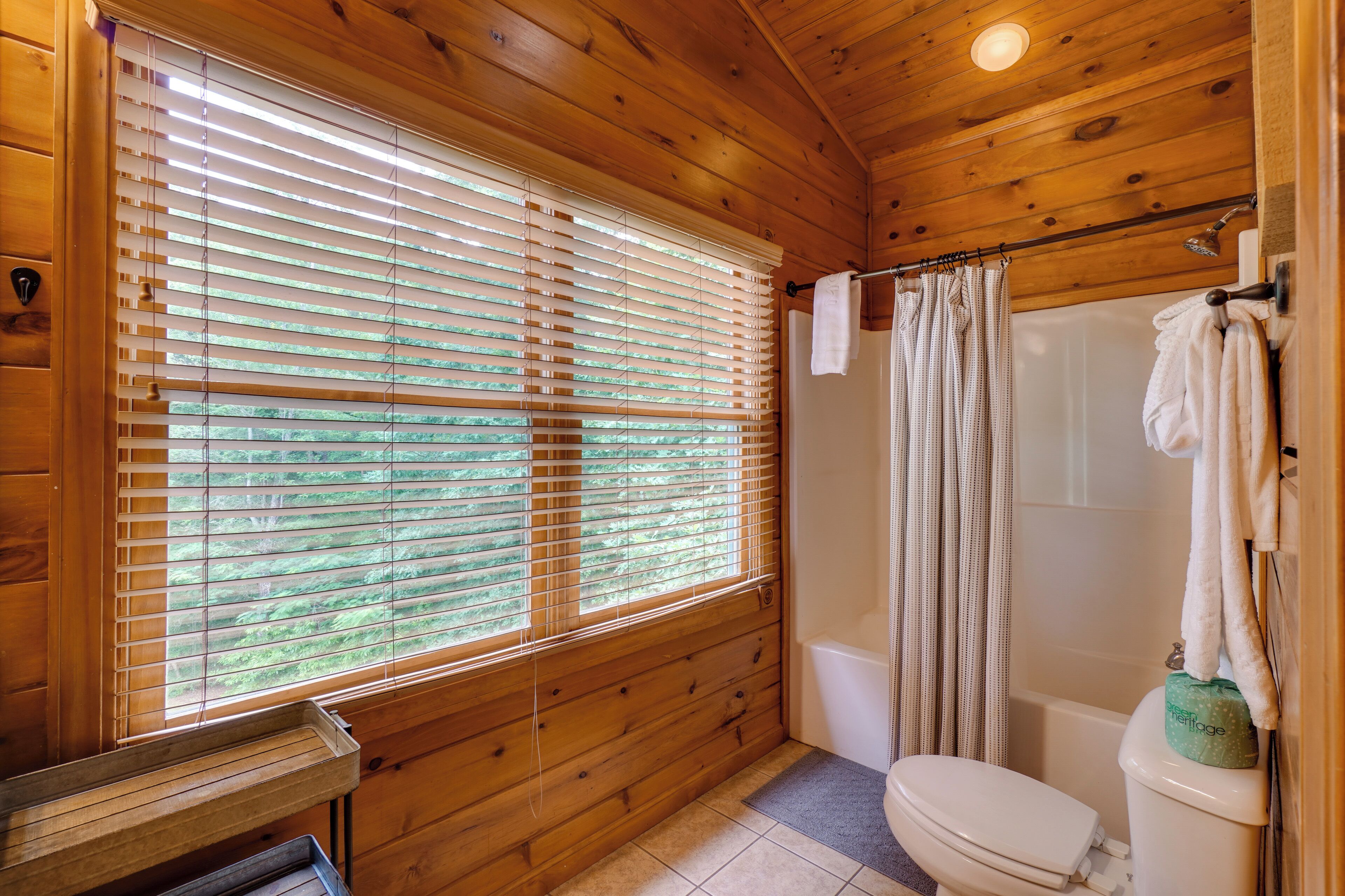 Een houten badkamer in een vakantiehuisje, met een toilet, douche en een raam met zonwering.