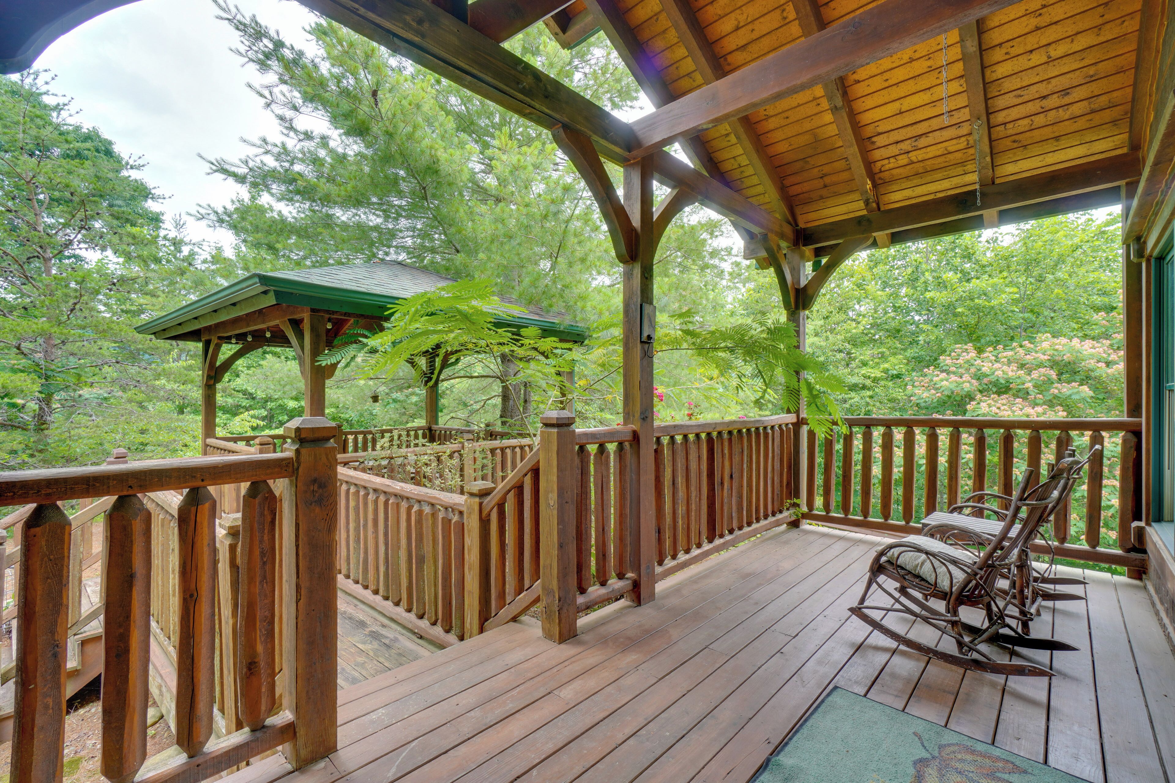 A wooden deck with a covered area, a rocking chair, and a gazebo.