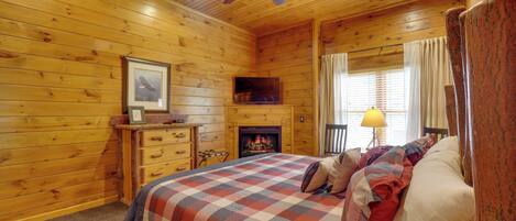 Ein Blockhausszimmer mit einem Bett, Holzwänden, einem Kamin, einem Deckenventilator und einem Fenster mit Vorhängen.