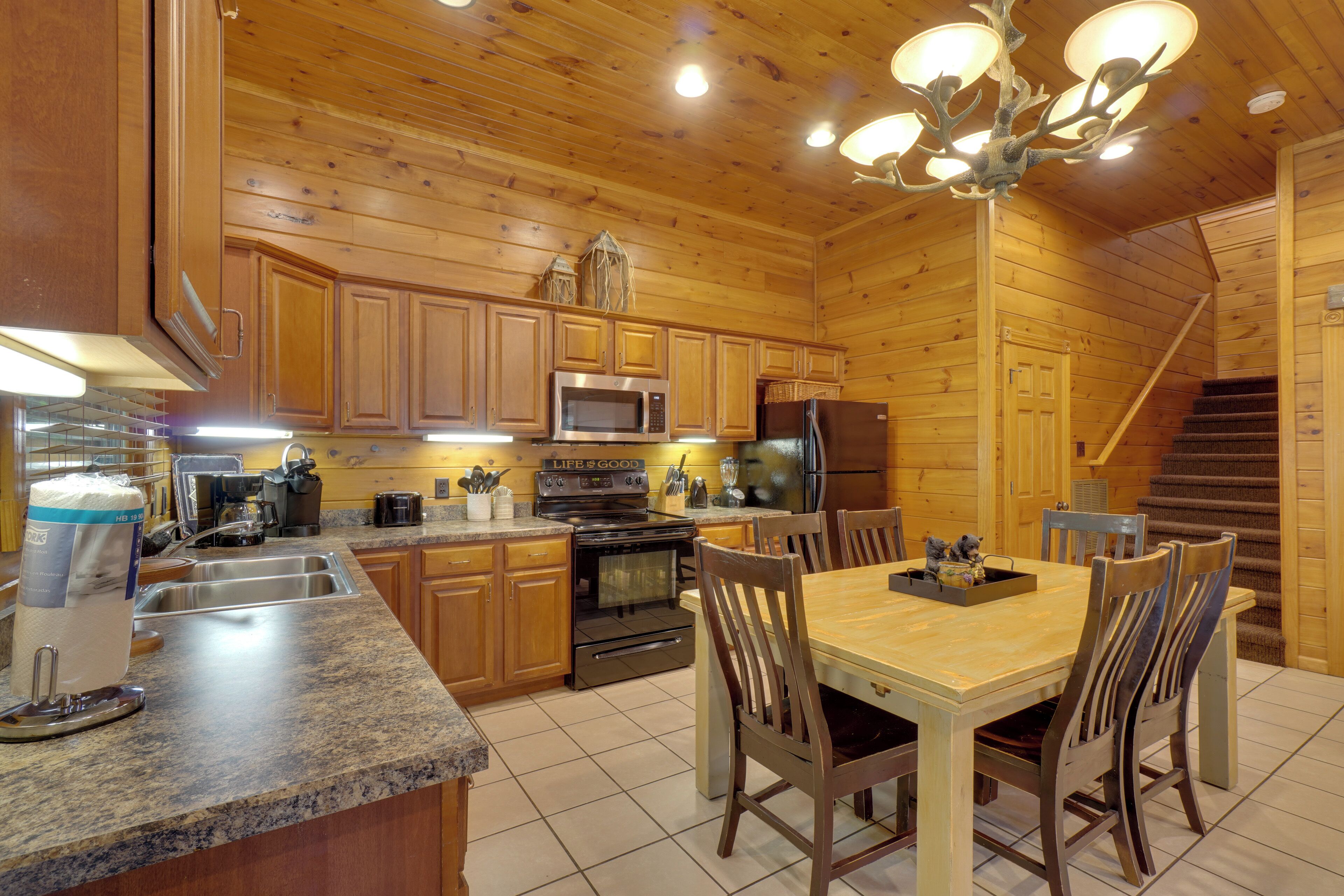 A wooden cabin kitchen with granite countertops, wooden cabinets, a stainless steel microwave, a refrigerator, and a dining table with chairs.