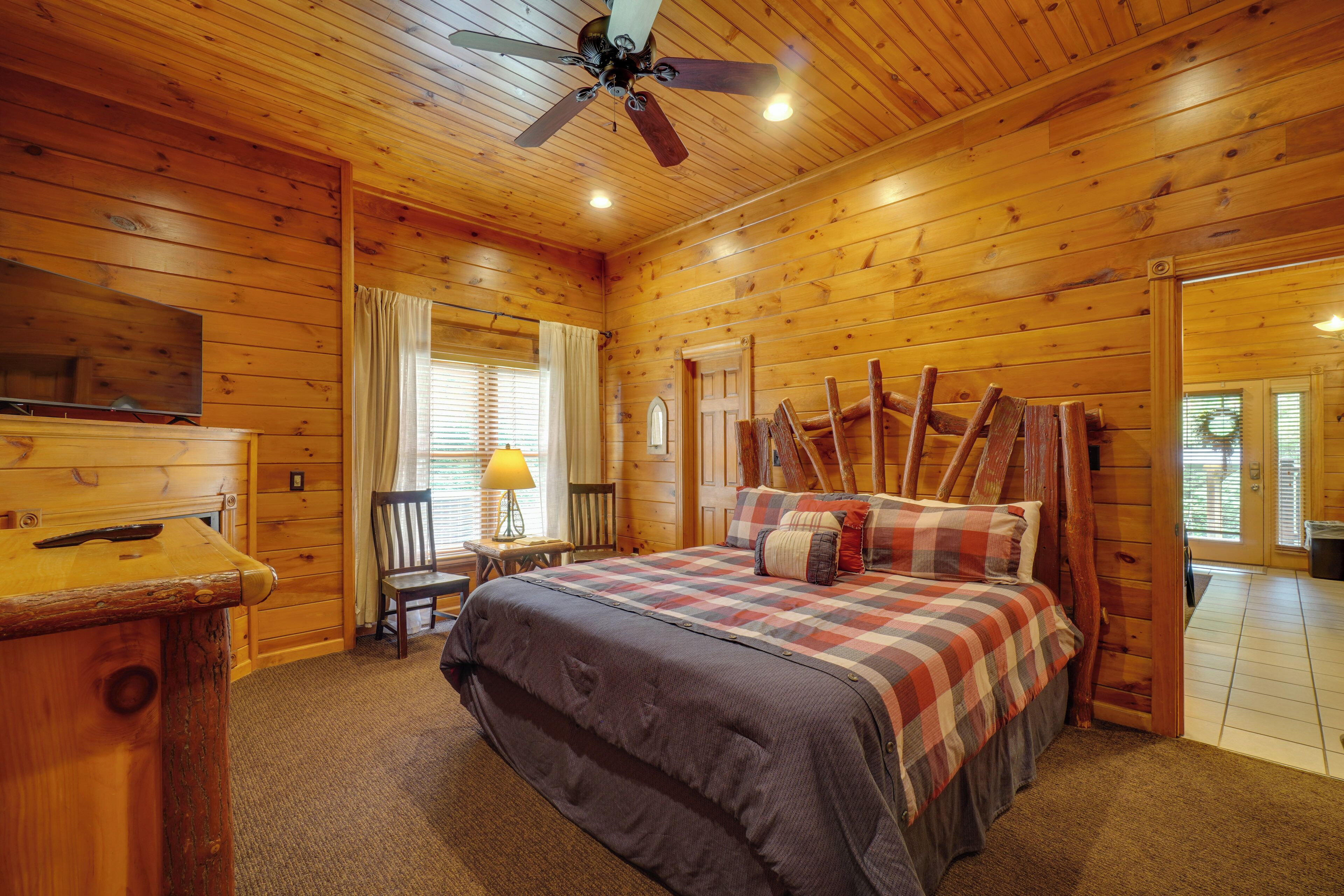 A wooden cabin bedroom with a bed, a ceiling fan, a desk, and a chair.