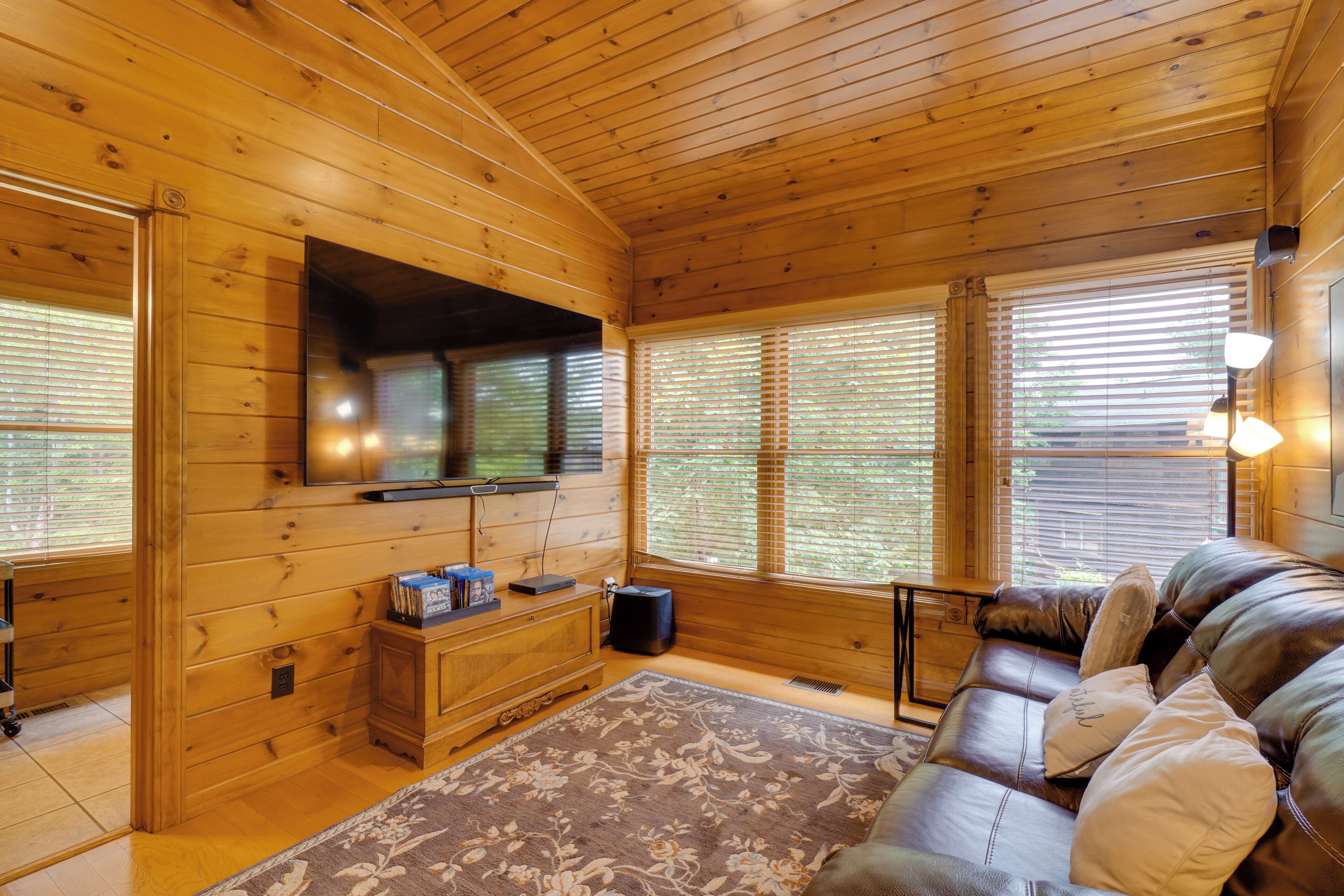 A wooden cabin interior with a sofa, TV, and windows.
