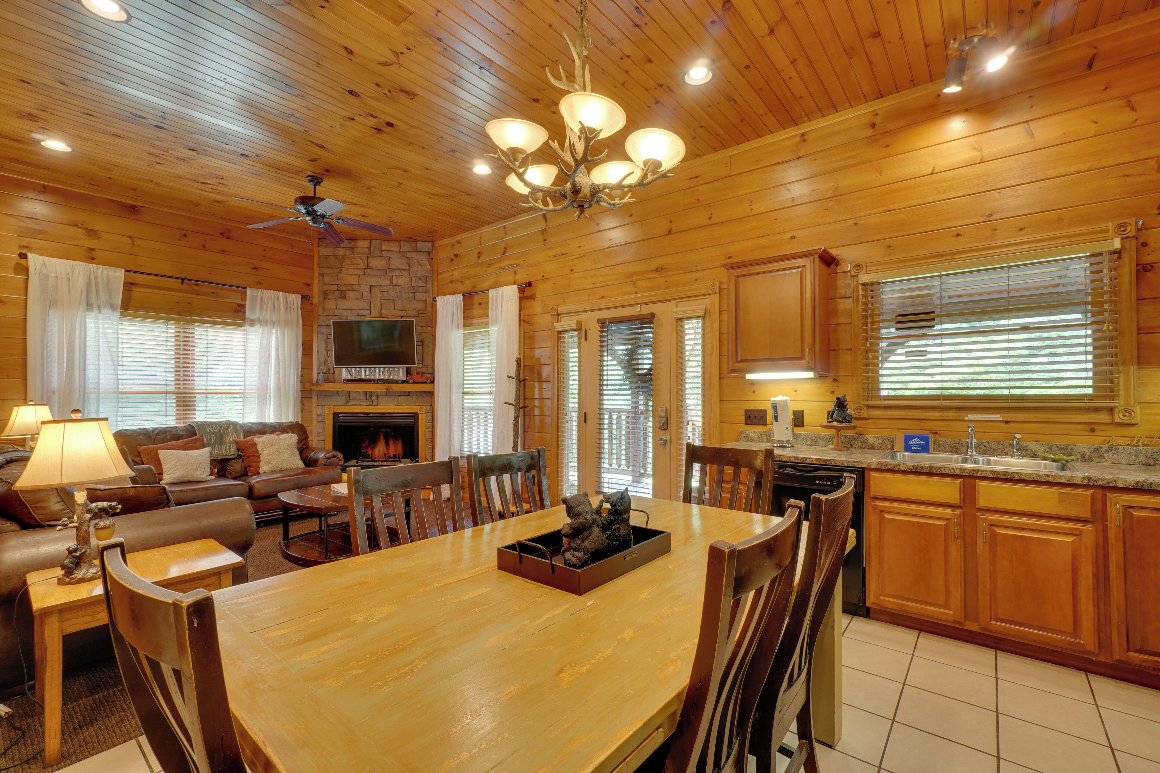 A wooden interior with a dining table, chairs, a fireplace, a television, and a kitchen area.
