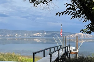 Un muelle se adentra en un lago tranquilo con montañas al fondo.