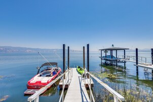A dock with a red speedboat and a green kayak, a covered structure, and calm water with distant mountains.