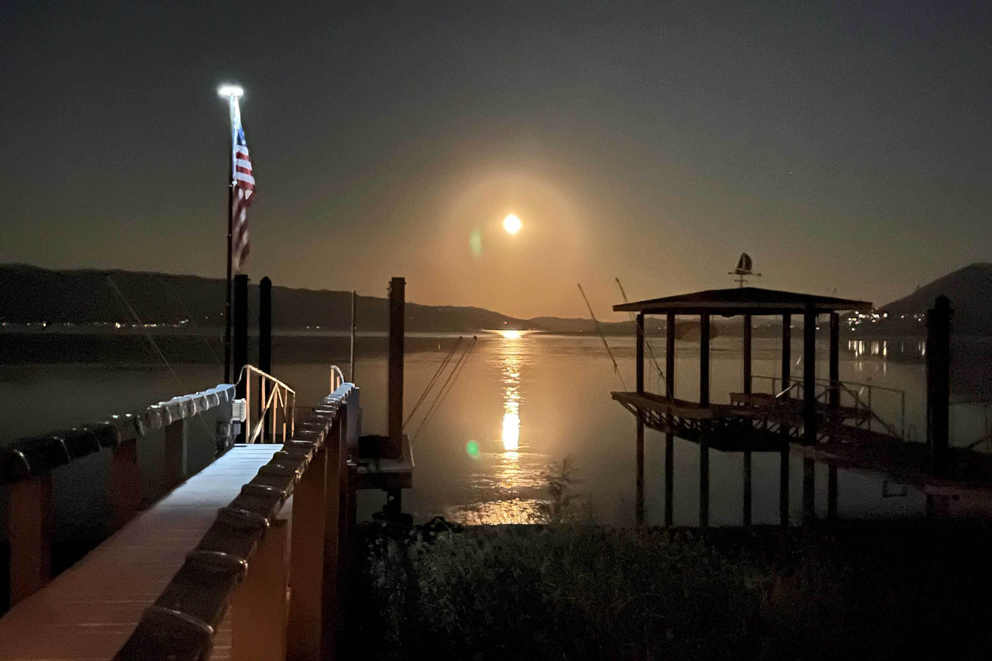 A nighttime view of a waterfront with a dock, a gazebo, and an American flag.