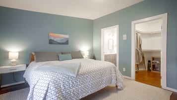 A bedroom with a bed, nightstands, a painting, a bathroom with a mirror, and a closet.